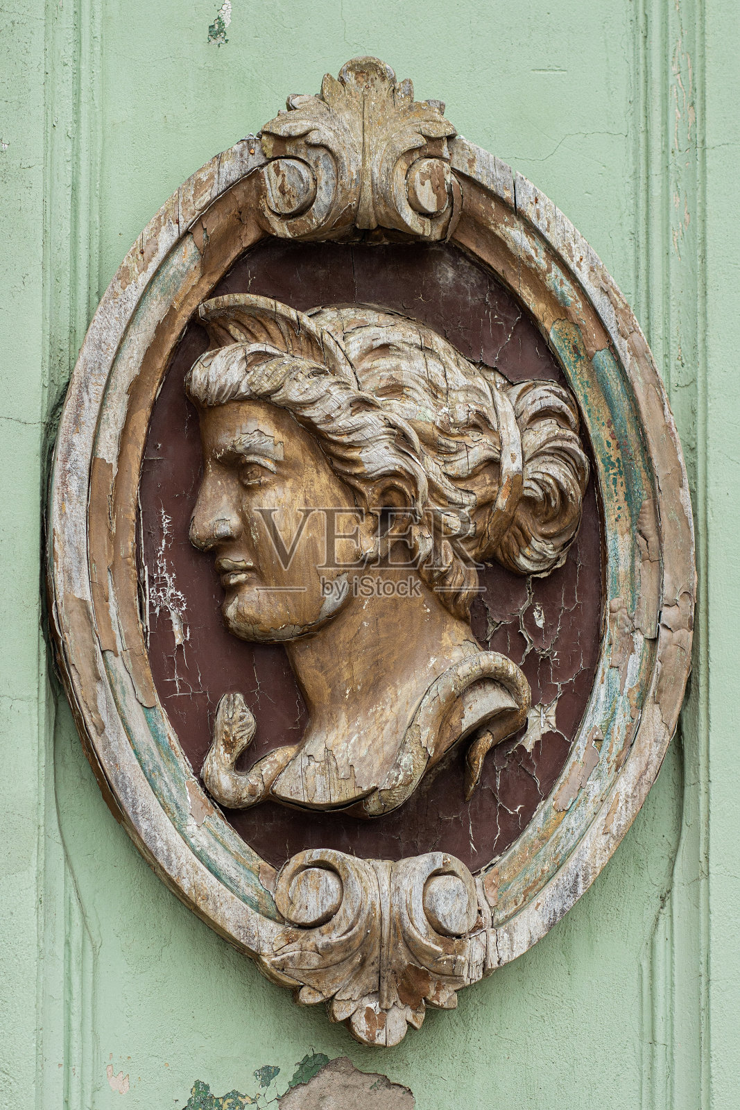 椭圆形装饰框中的女性头部木制雕塑，古老且饱经风霜，在旧建筑上装饰性浮雕照片摄影图片