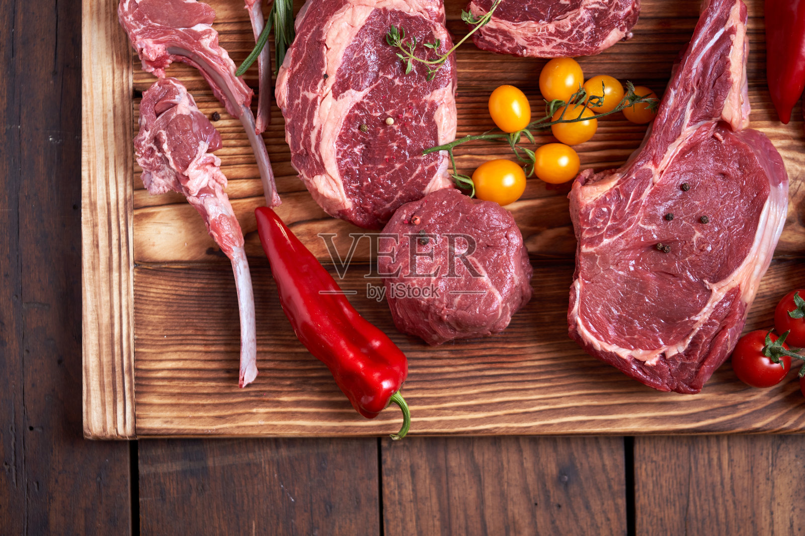 准备各种各样的烹饪肉类材料-小牛，肋眼，羊排，大蒜，洋葱，红色和黄色的西红柿，红辣椒，花椒，迷迭香，橄榄油，用猎刀在切木板上照片摄影图片