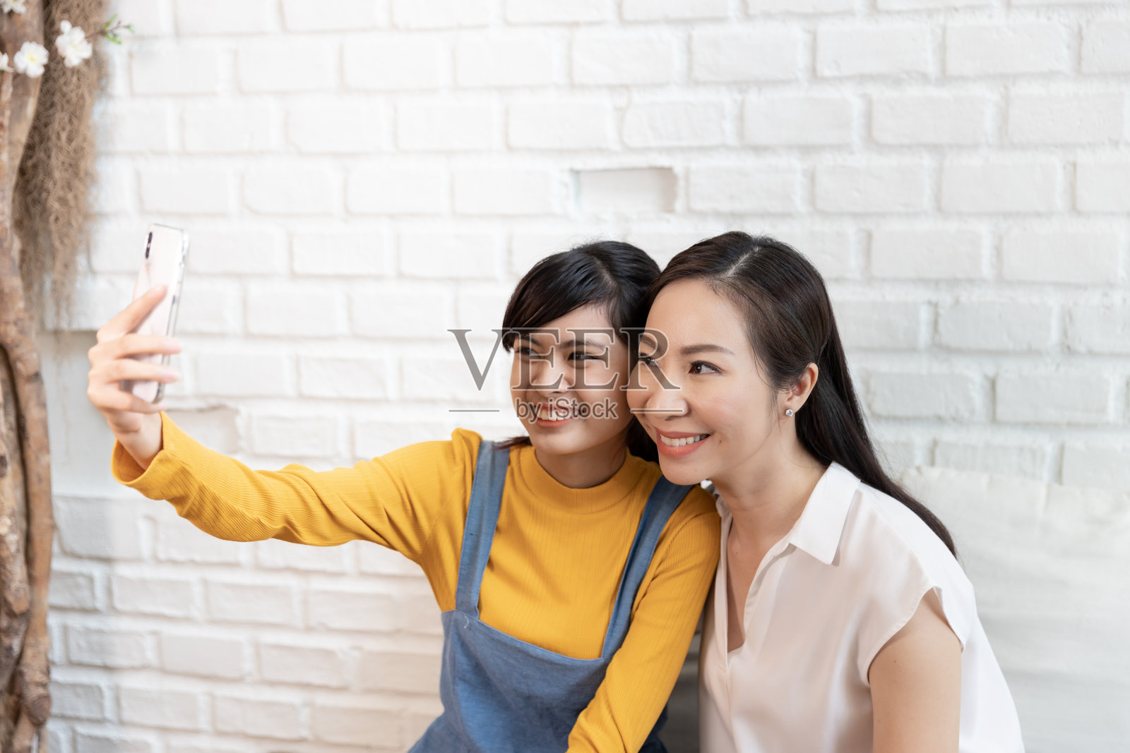 快乐的亚洲家庭妈妈和十几岁的女儿在家里有自然阳光的房间里给自己拍张照片，自拍或用智能手机打视频电话。照片摄影图片