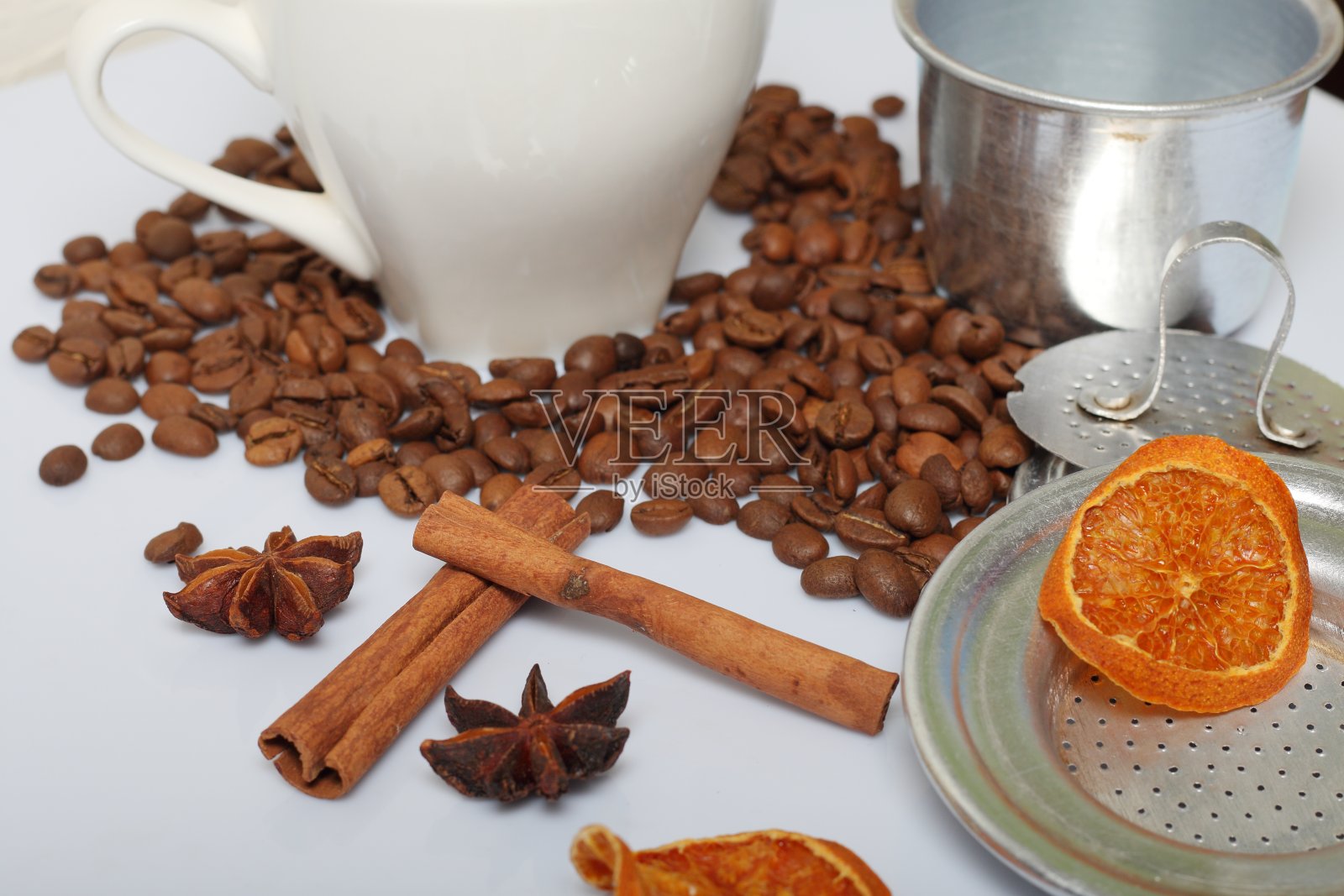 咖啡豆，肉桂棒，多香果和茴芹。旁边放着一个白色的杯子和几片干橙子。在白色背景上。世界咖啡的一天。照片摄影图片