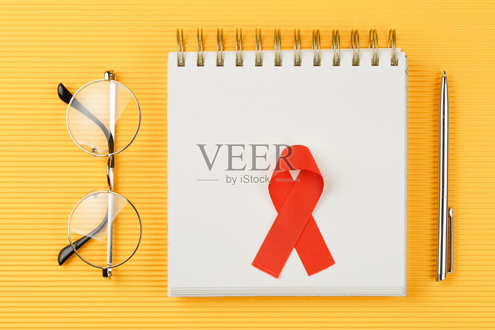 红色AIDS丝带在打开的笔记本上孤立在黄色的背景上照片摄影图片