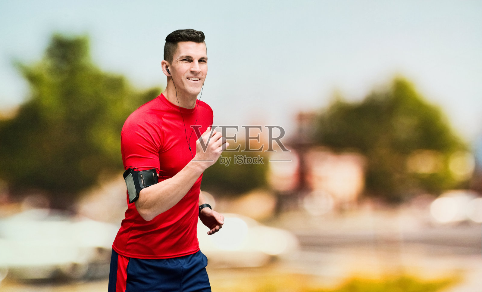 一个男人/一个人/腰部以上/侧视图/侧面视图30-39岁的成年人英俊的人白人男性/年轻男子在自然公园前锻炼，穿着t恤/衬衫谁是微笑/快乐/愉快/听照片摄影图片