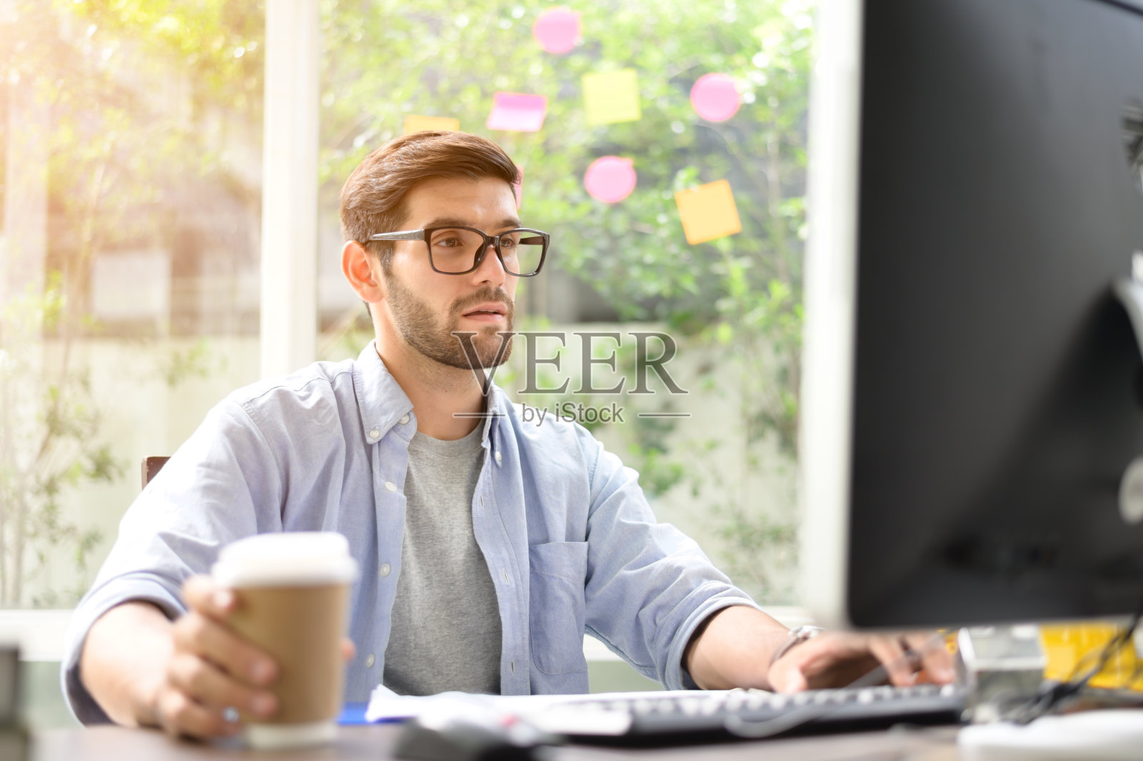 一个年轻人坐在家里的电脑屏幕前，喝着一杯咖啡。照片摄影图片