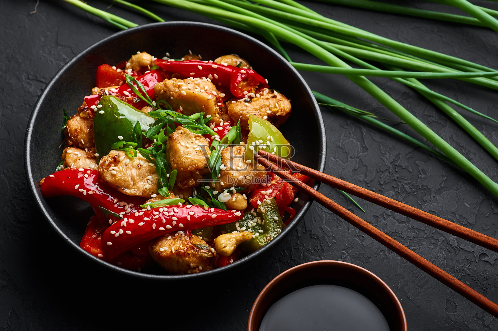 黑碗四川鸡或龙鸡，暗板背景。四川鸡是一种很受欢迎的印支菜，以辣椒、鸡肉和蔬菜为主。照片摄影图片