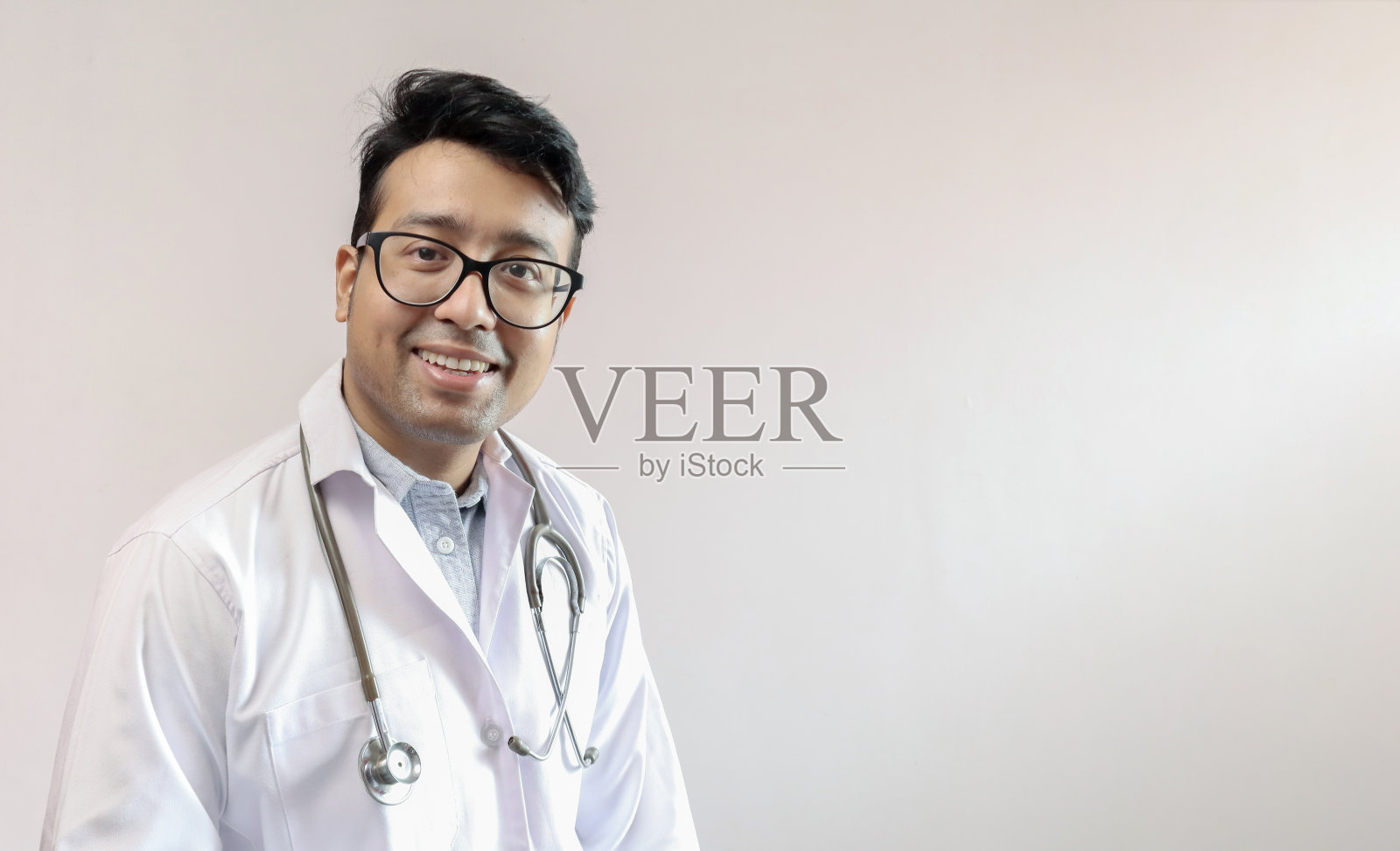 穿着白大褂和听诊器的印度男性医生，在白色背景中留出文字空间照片摄影图片