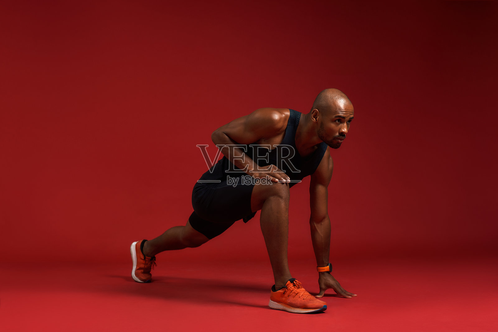 训练前的热身。年轻和强壮的非洲男子在运动服装伸展，而站在红色的背景照片摄影图片
