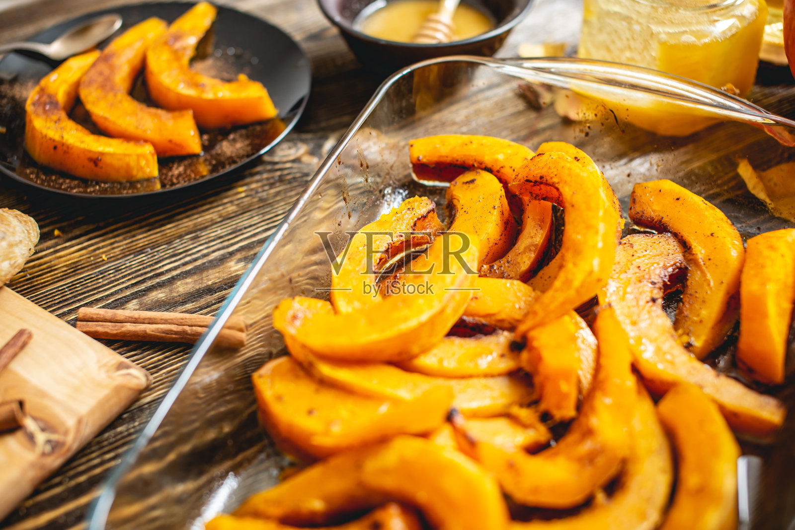 木桌上放着几片烤好的橙色南瓜、蜂蜜和肉桂。作为秋天的一道甜点照片摄影图片