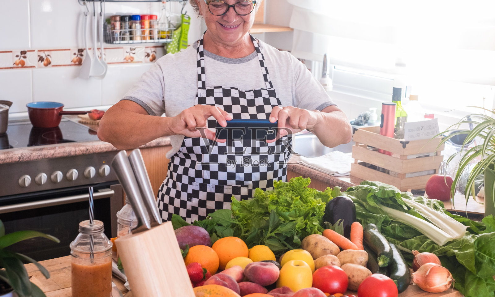 一位老年妇女用手机拍了一张桌子上有一大群五颜六色的水果和蔬菜的照片。健康饮食照片摄影图片