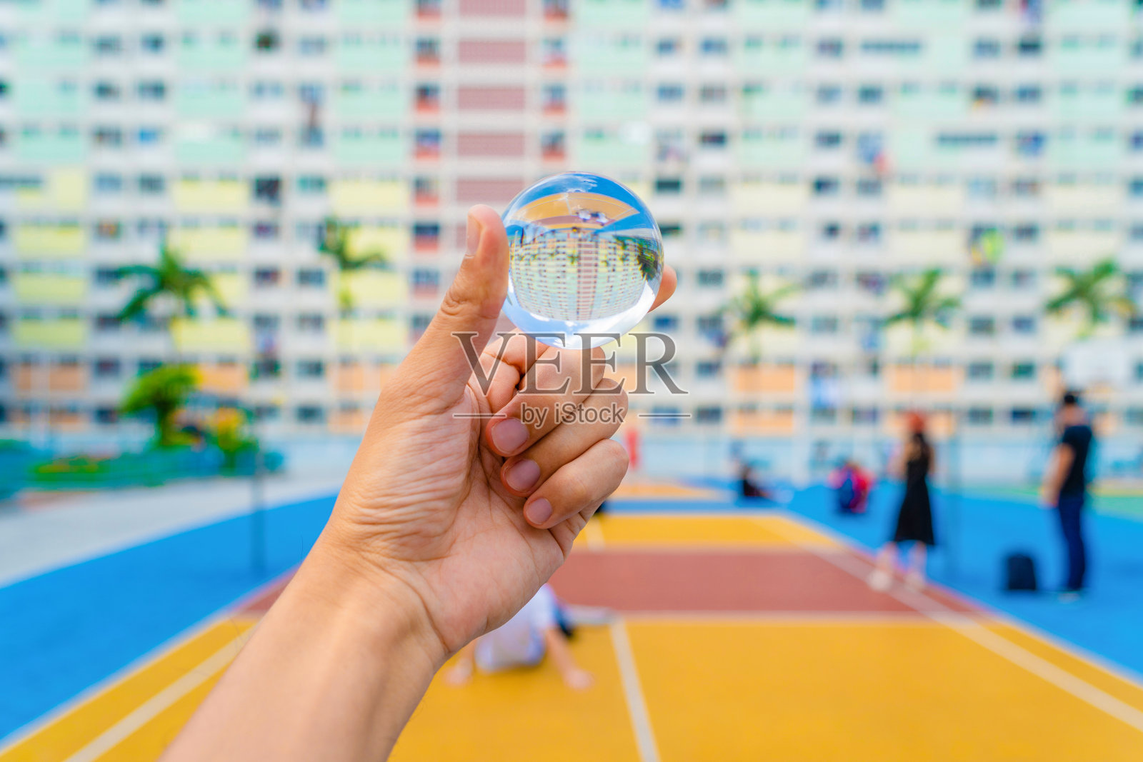 在中国香港市区的公园里，在旅游假期旅行期间，拿着一个玻璃或水晶球在五颜六色的彩虹色调的建筑里，有篮球场和正面的窗户。照片摄影图片