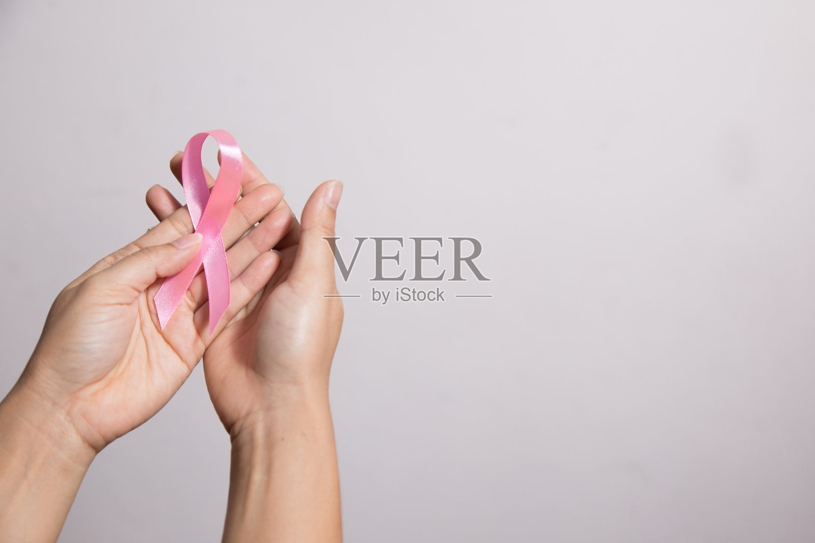 粉红丝带，以提高女性乳腺癌患者对乳腺癌的认识。拿着粉红丝带的女人。癌症的认识概念。照片摄影图片
