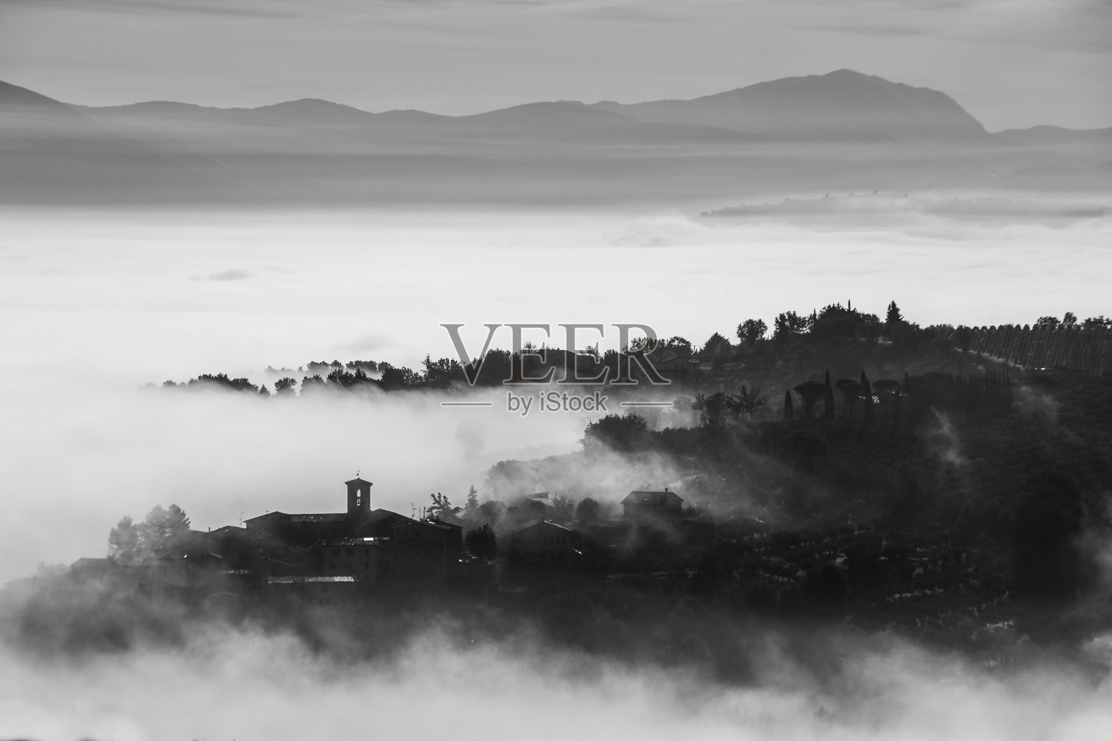 在翁布里亚(意大利)一个几乎完全被雾掩盖的小镇的超现实的观点照片摄影图片