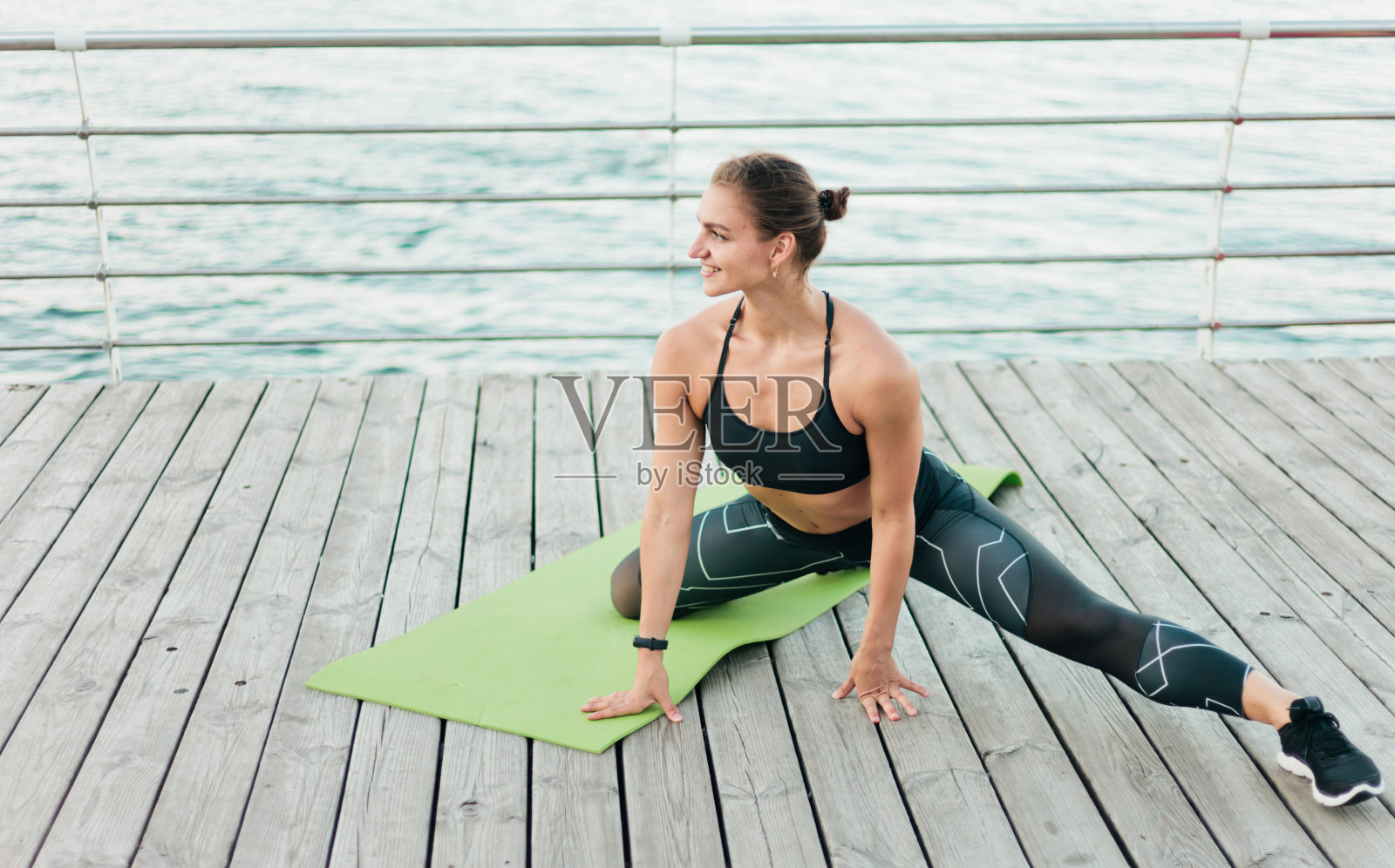可爱的肌肉女运动员在运动服表演她的身体做腿伸展在一个海滩平台。户外训练照片摄影图片