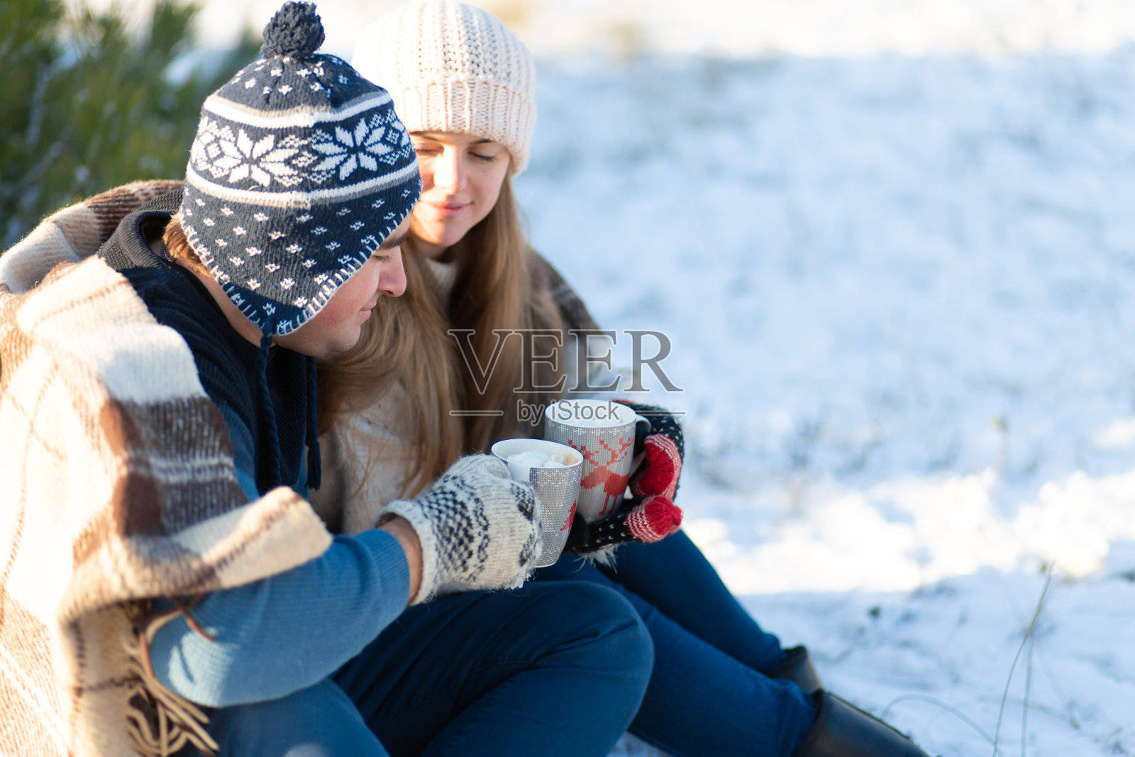 相爱的年轻情侣用棉花糖喝热饮，坐在冬天的森林里，躺在温暖舒适的地毯里，享受大自然照片摄影图片