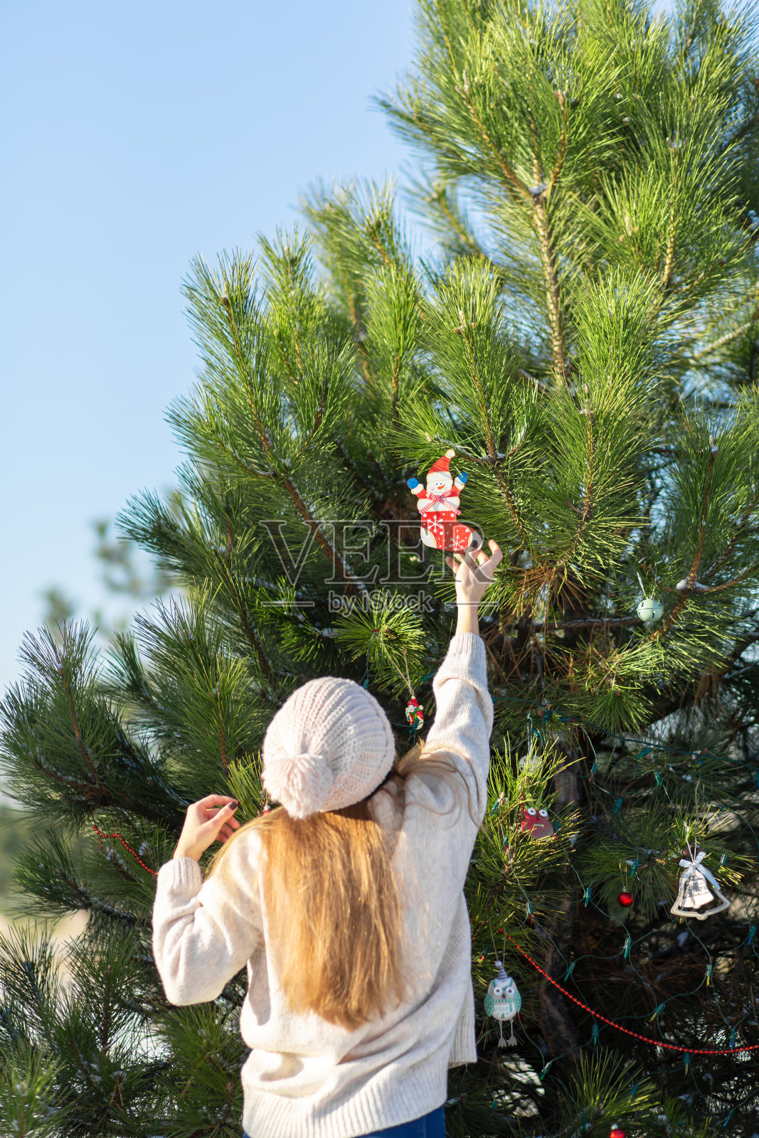冬天，在森林里的街道上，女孩用装饰性的玩具和花环装饰一棵绿色的新年树。圣诞树装饰品照片摄影图片