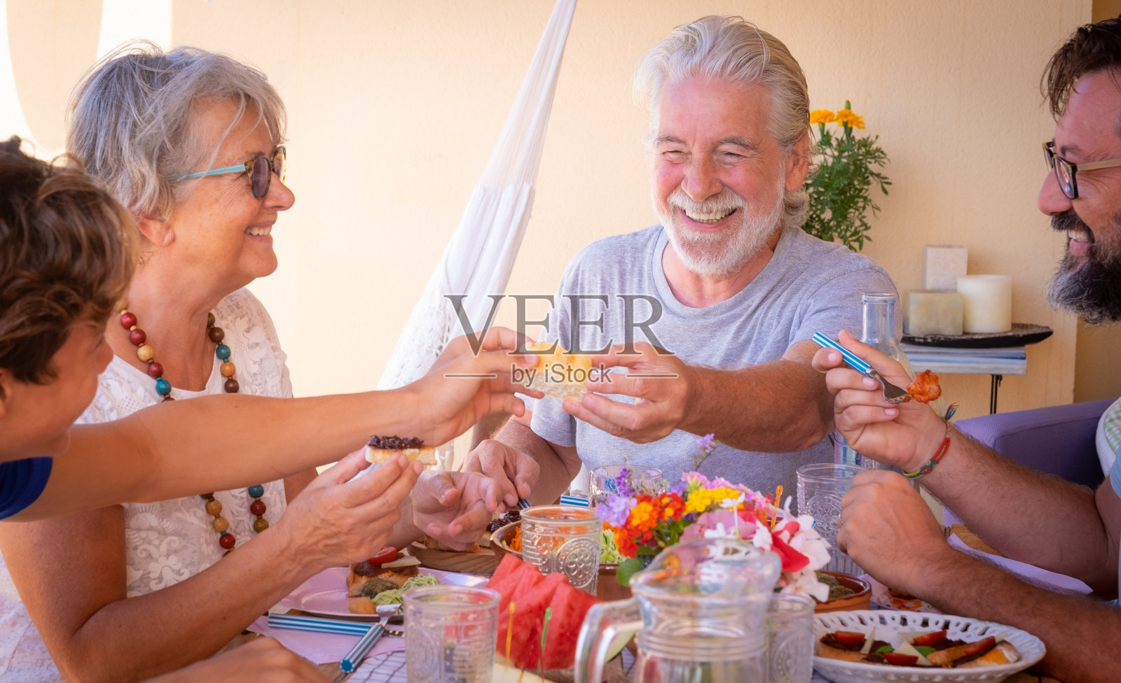 欢乐的一家人，三代同堂，一起在田埂上吃素食。老两口带着儿子和孙子的爷爷奶奶。明亮的阳光。木制的桌子照片摄影图片