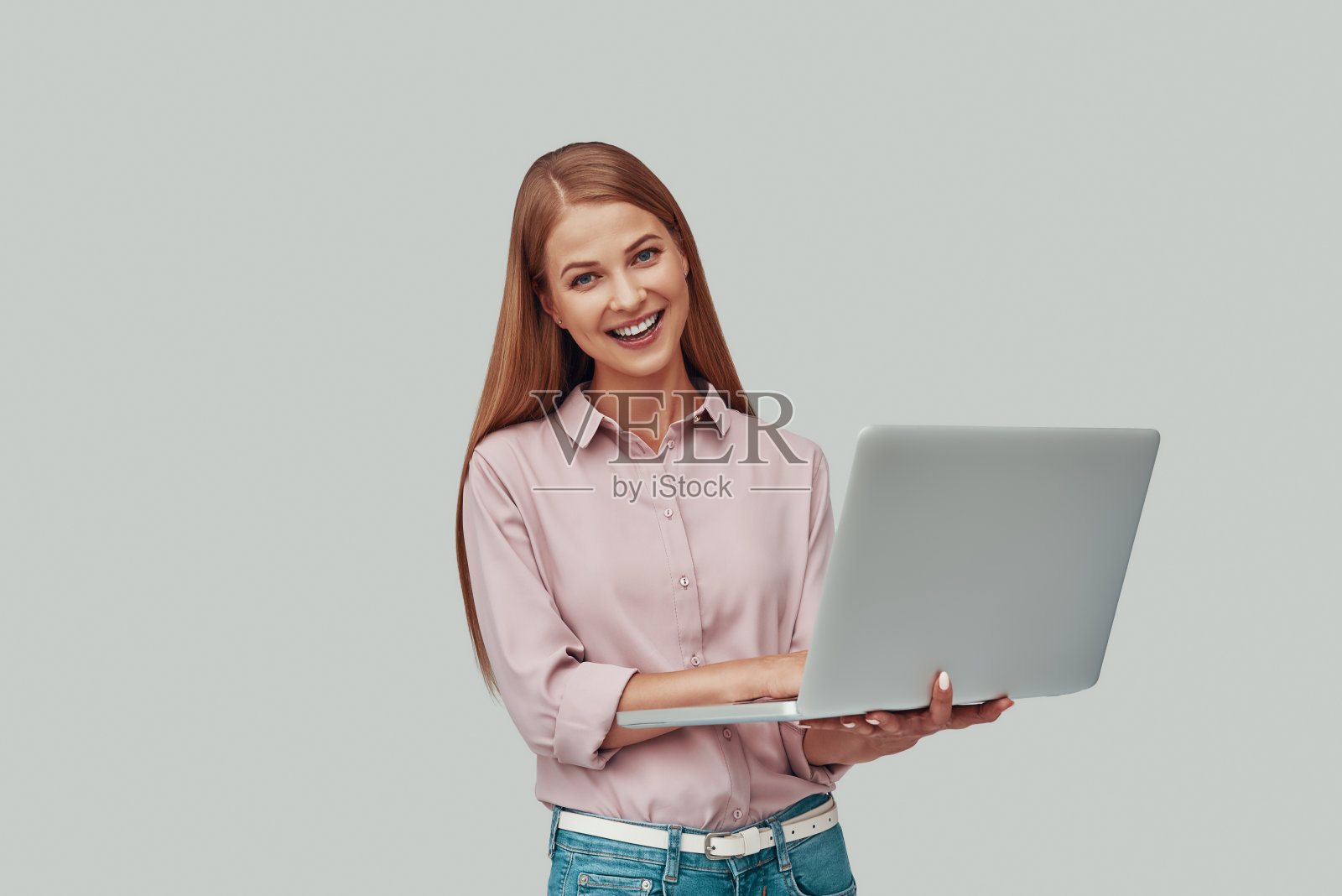 迷人的年轻女子使用笔记本电脑，微笑着站在灰色背景照片摄影图片