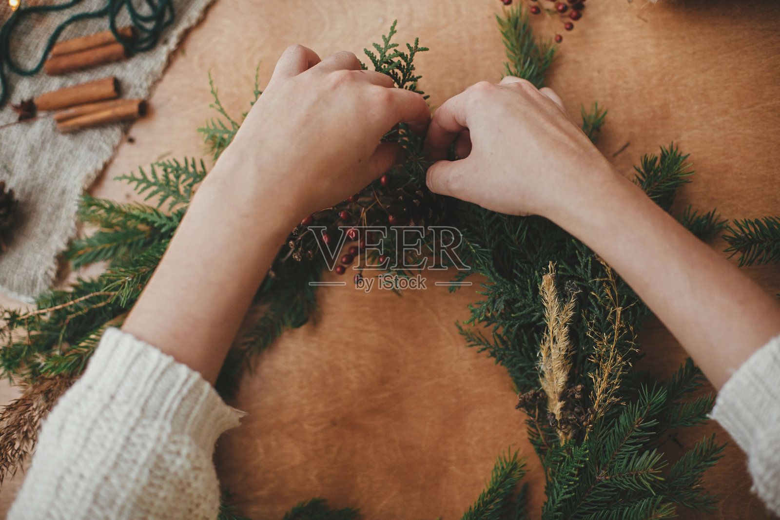 手里拿着冷杉树枝、松果、针线、浆果、剪刀放在木桌上。让乡村圣诞花环平躺。圣诞花环车间。真实时尚的静物照片摄影图片