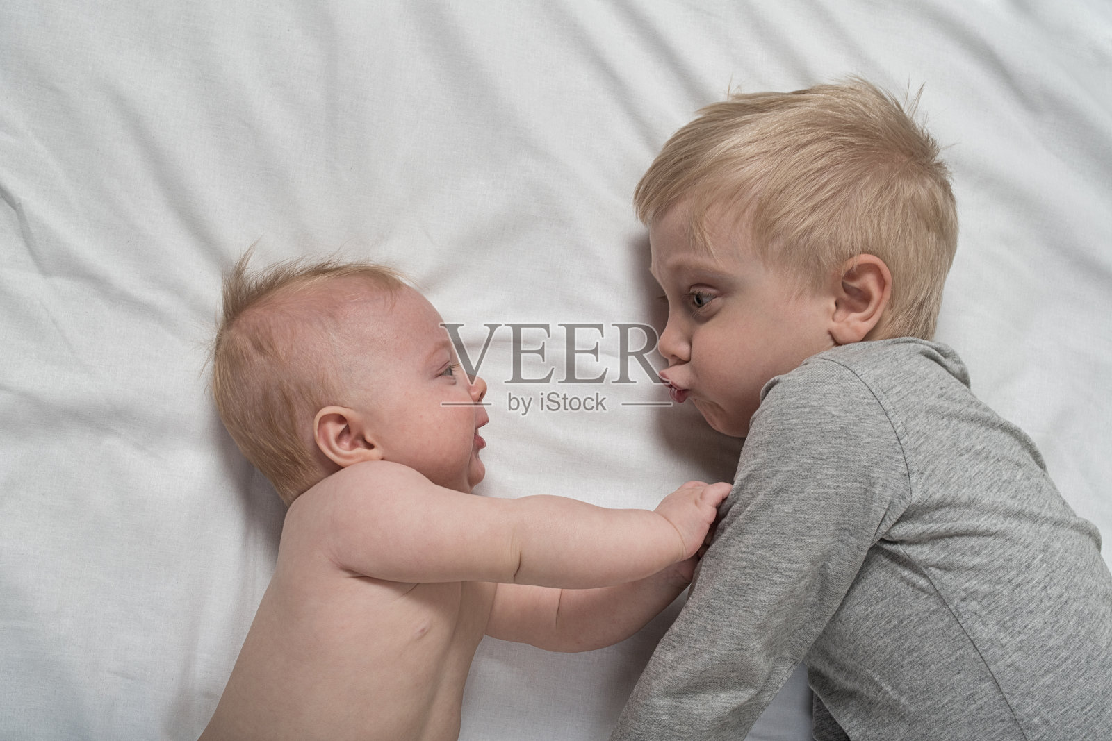 宝宝和笑眯眯的哥哥正躺在床上。他们玩耍，有趣，互动。俯视图照片摄影图片