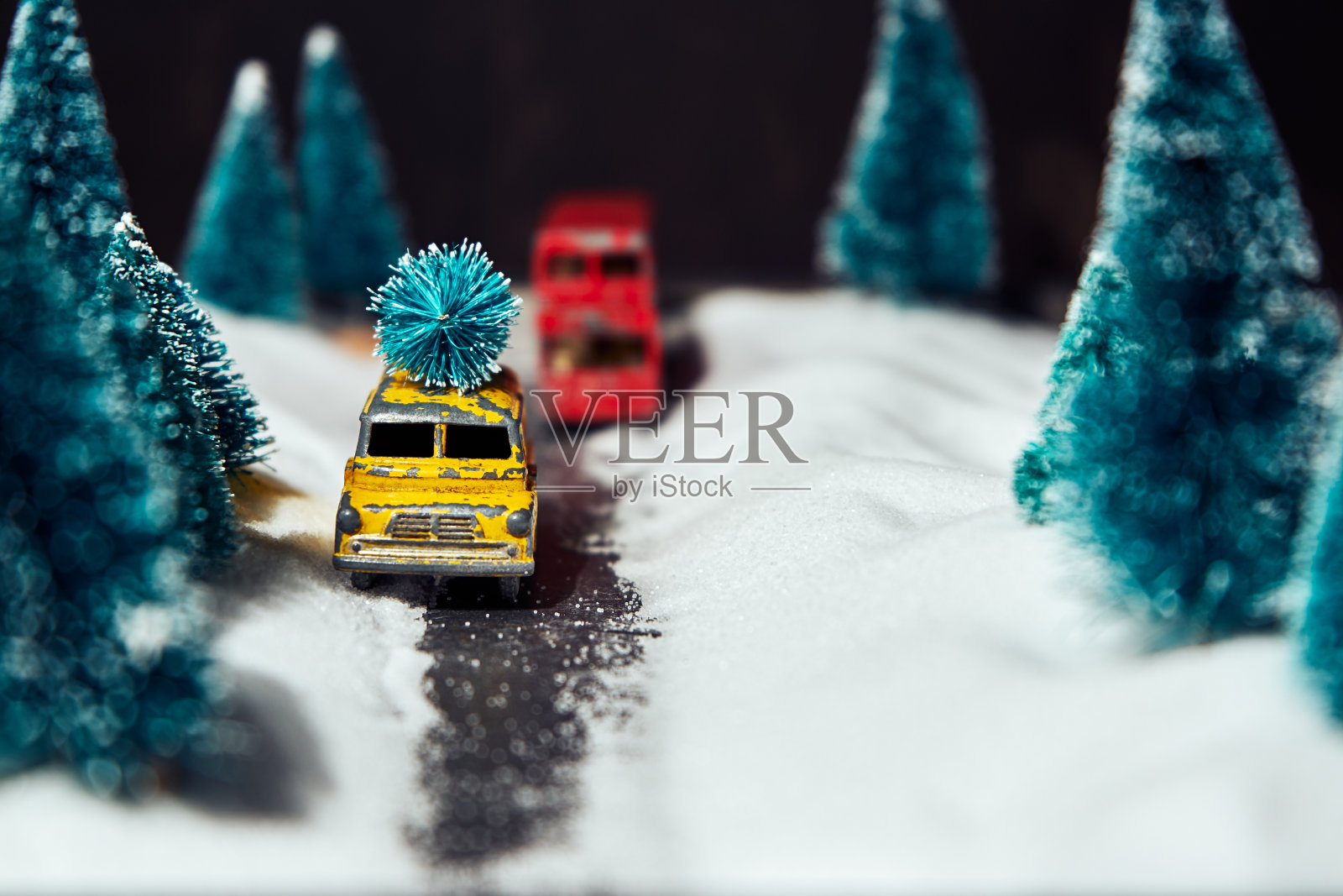 选择性的聚焦在黄色的玩具车上，车顶上有一棵圣诞树在模糊的模仿冬天的背景照片摄影图片