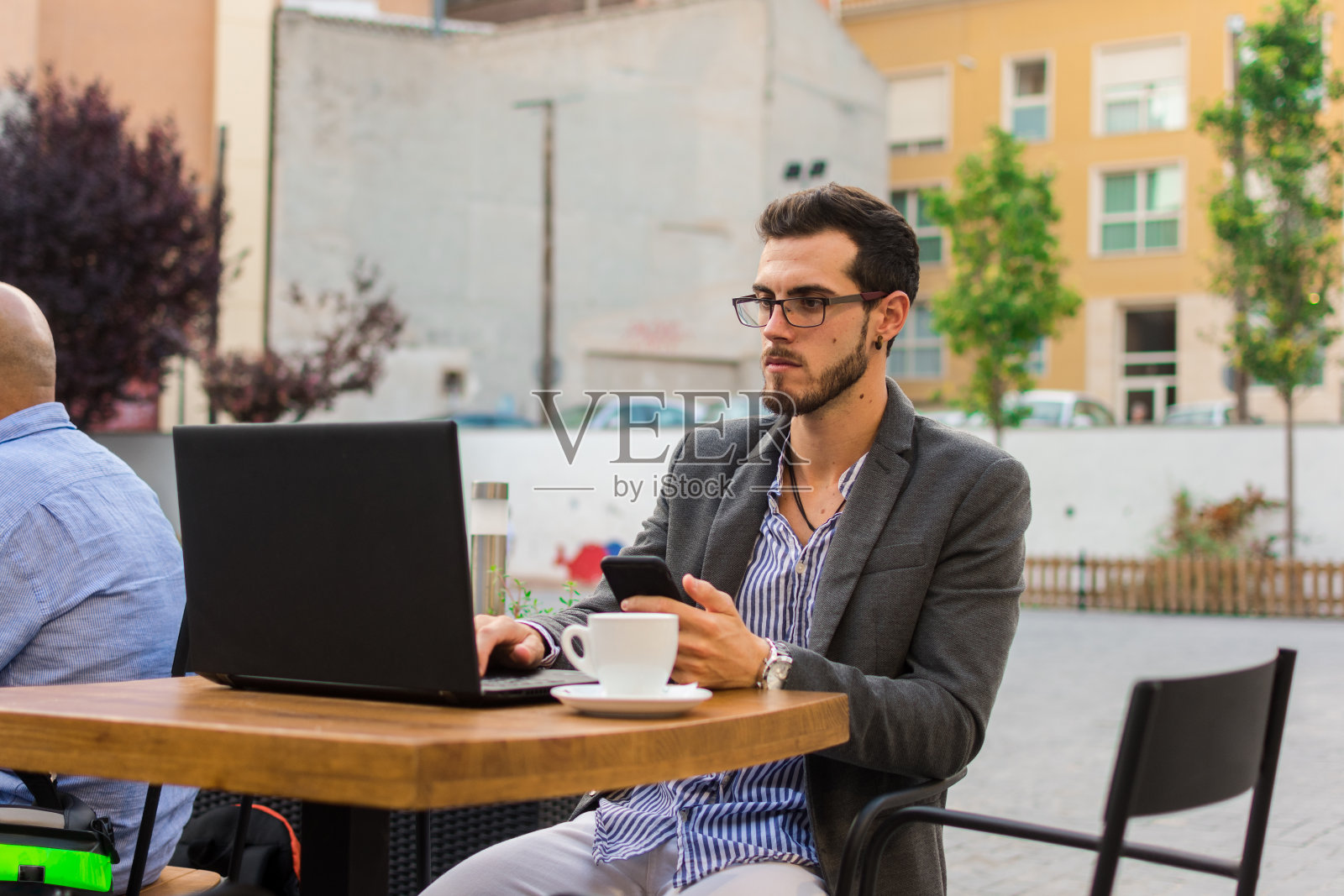 一个年轻的商人正在一个酒吧的露台上工作，他的笔记本电脑和智能手机照片摄影图片