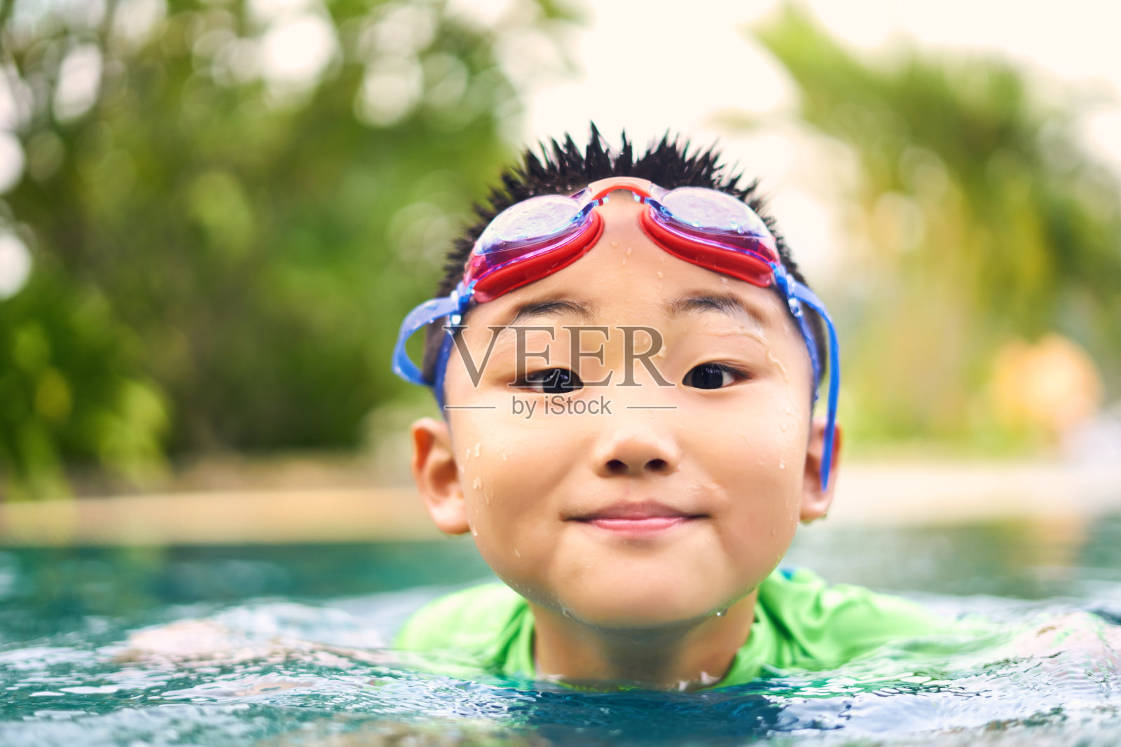 一个头戴红色护目镜的中国男孩在泳池里对着镜头微笑照片摄影图片