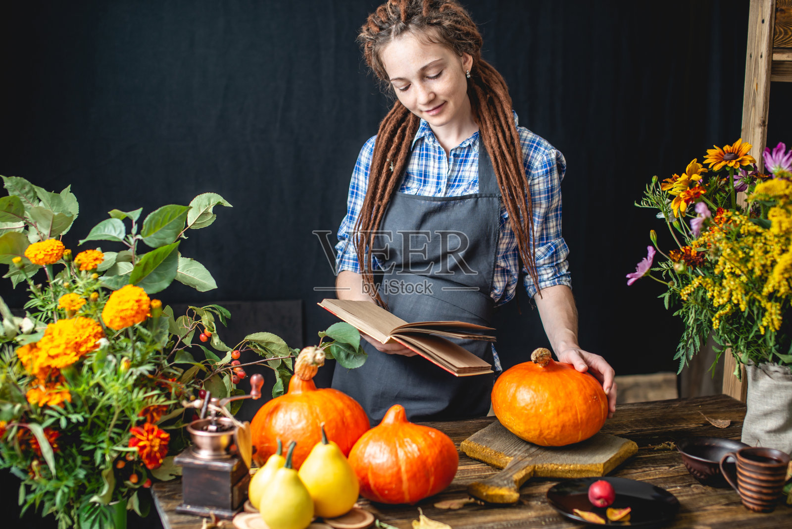 女厨师在一本烹饪橘色南瓜的书里读食谱。概念秋季食物在一个舒适的深色木制厨房照片摄影图片