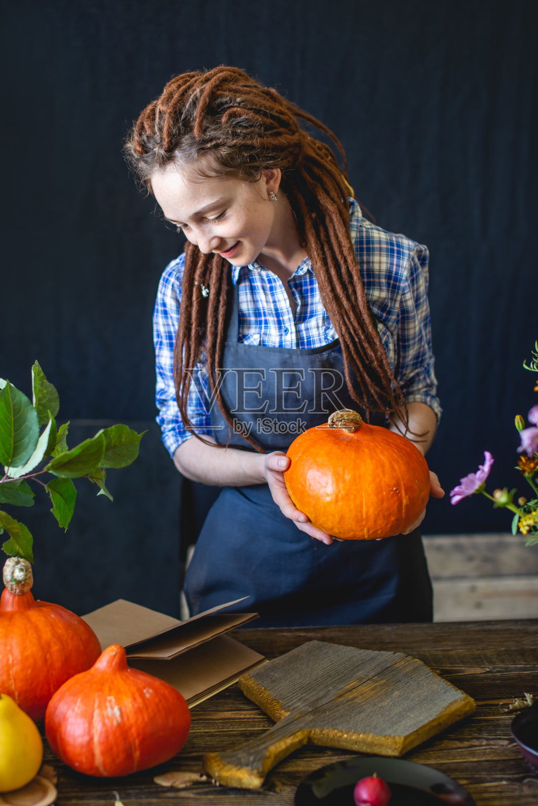 女厨师在一本烹饪橘色南瓜的书里读食谱。概念秋季食物在一个舒适的深色木制厨房照片摄影图片
