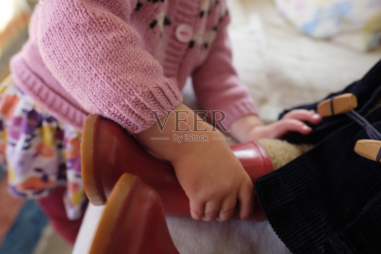 一个小孩把一只红色的靴子推到一个玩具泰迪上照片摄影图片