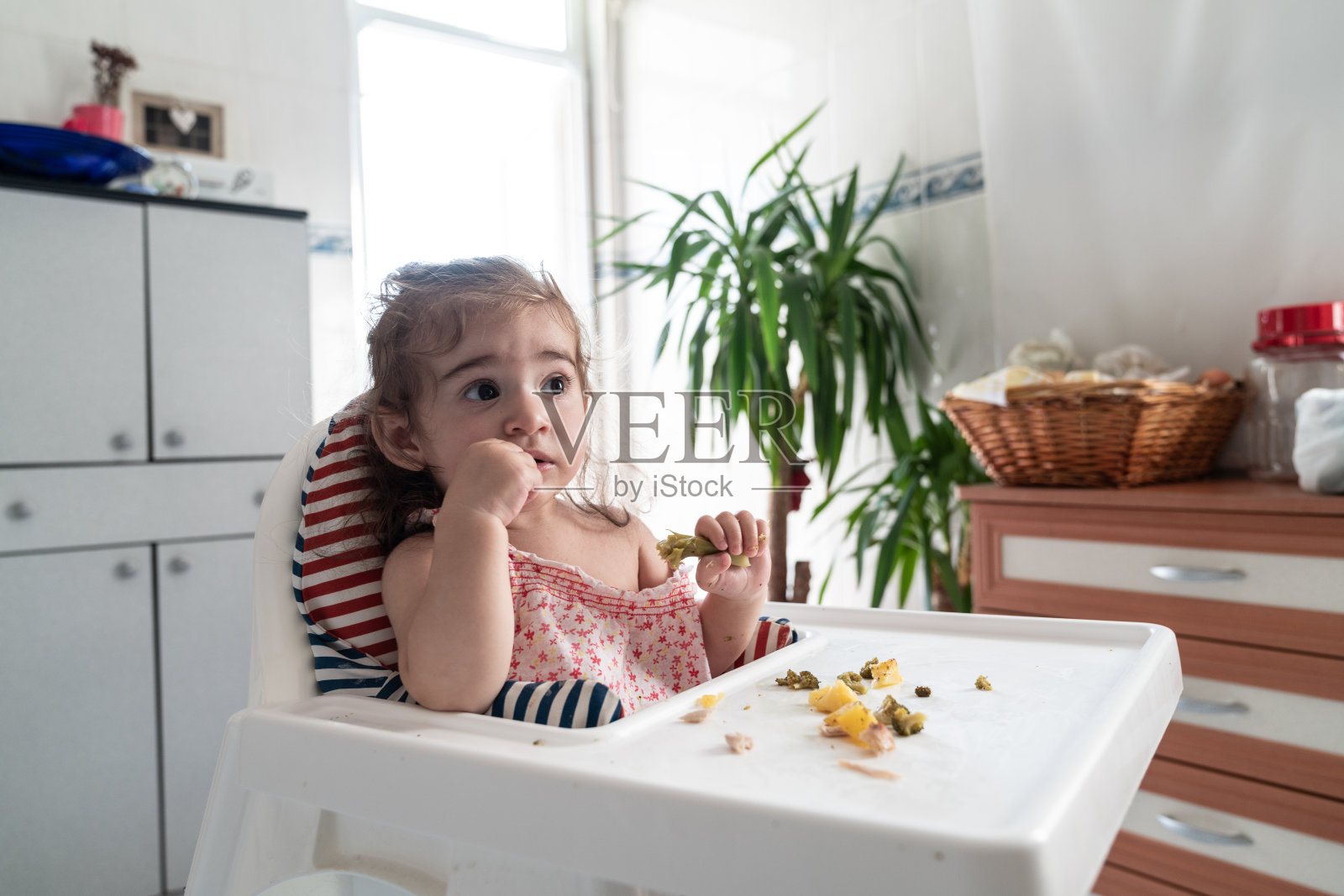 蹒跚学步的小女孩坐在喂食椅上吃食物照片摄影图片