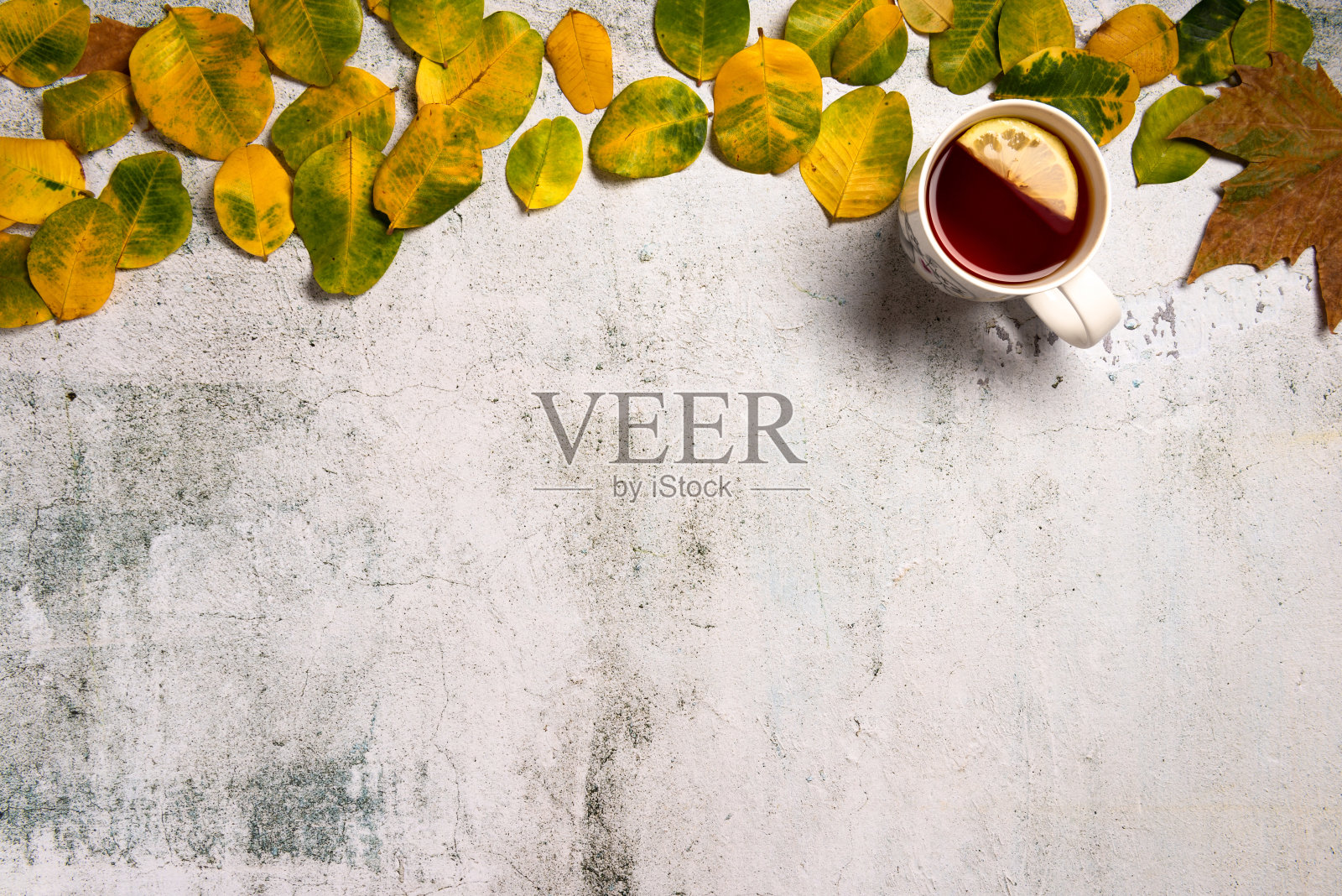 一杯热茶点缀着黄色的秋叶，映衬着灰色的纹理背景。平躺照片摄影图片