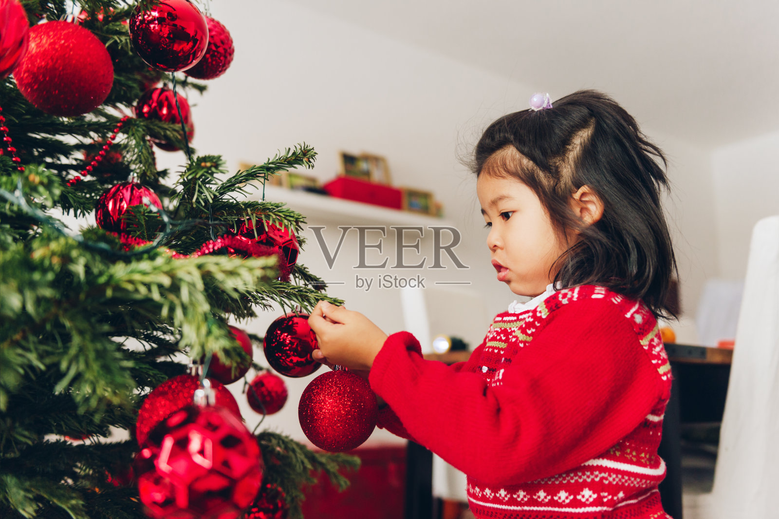 可爱的3岁小女孩穿着红色套衫装饰圣诞树照片摄影图片
