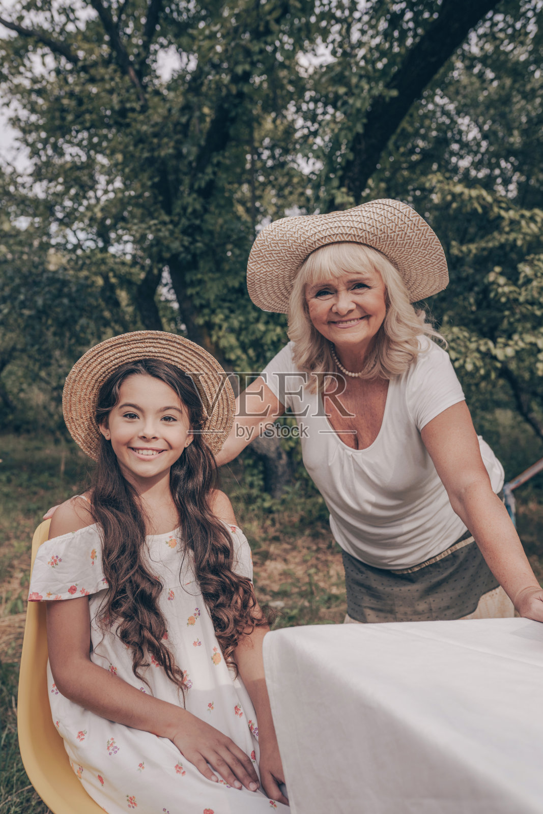 美丽的肖像，一个老祖母和她的孙女在花园里。一个幸福的家庭。这孩子去拜访一位老妇人。愉快地坐在桌边，微笑着。幸福生活的秘诀照片摄影图片