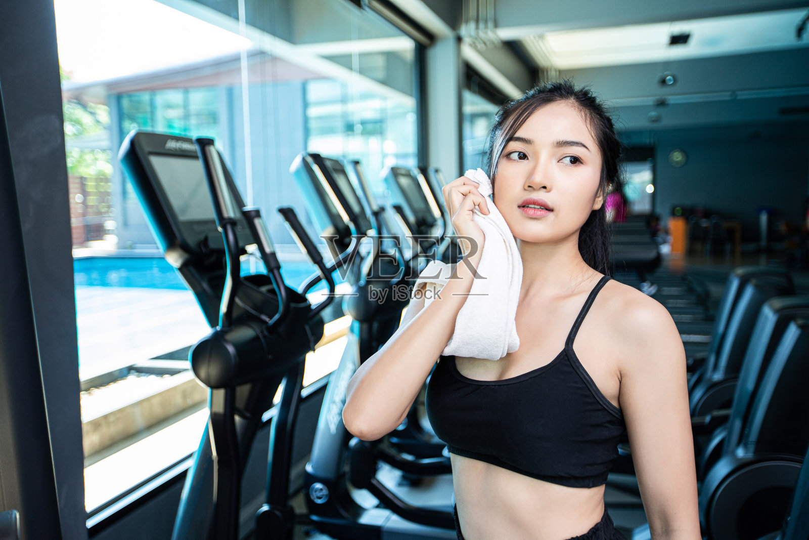 女性锻炼后，在健身房用一块白布擦脸。照片摄影图片