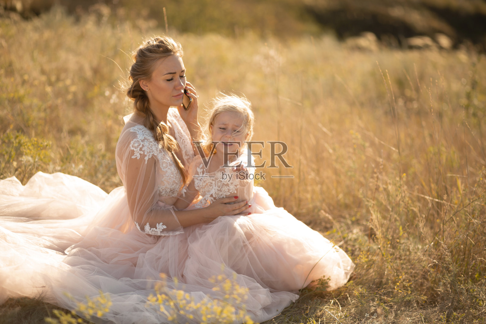 一个小女孩在她妈妈打电话的时候哭了。妈妈和女儿正坐在地里照片摄影图片