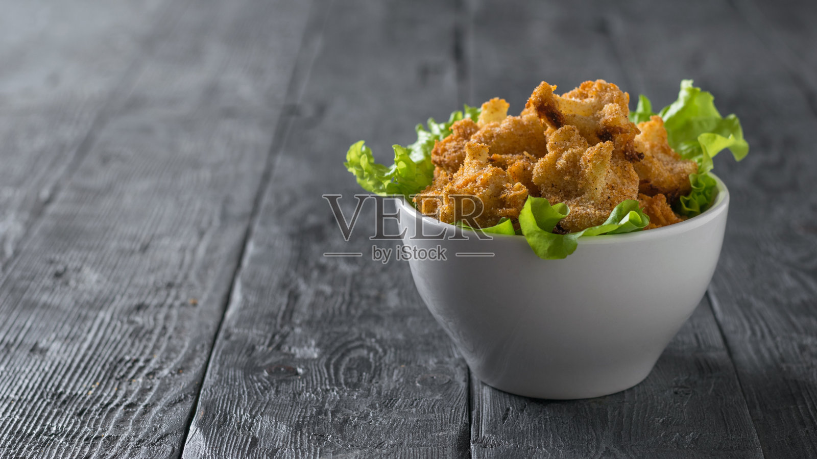 木桌上放着一只白色的碗，上面放着烤好的花椰菜和莴苣。照片摄影图片