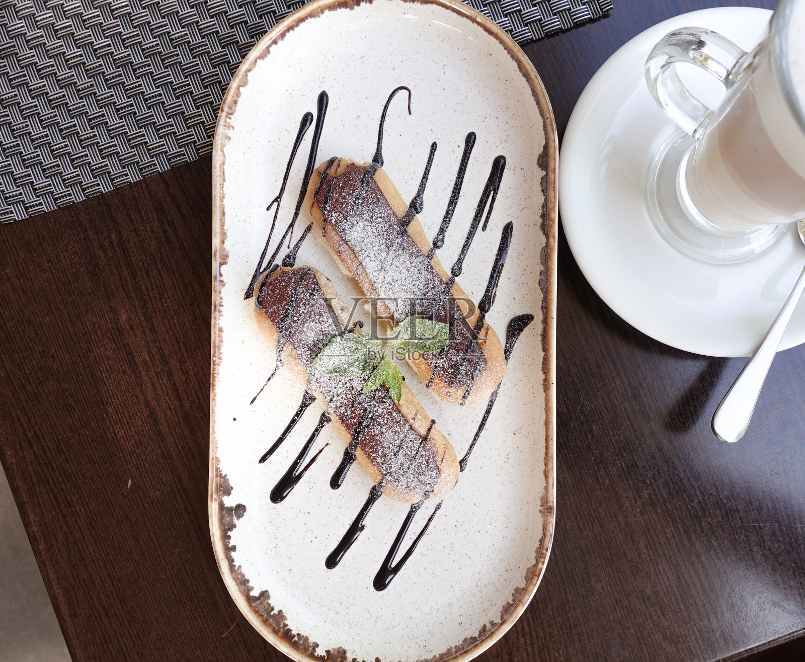 两个美味的泡芙，放在浸满巧克力的盘子里。从上面的观点照片摄影图片