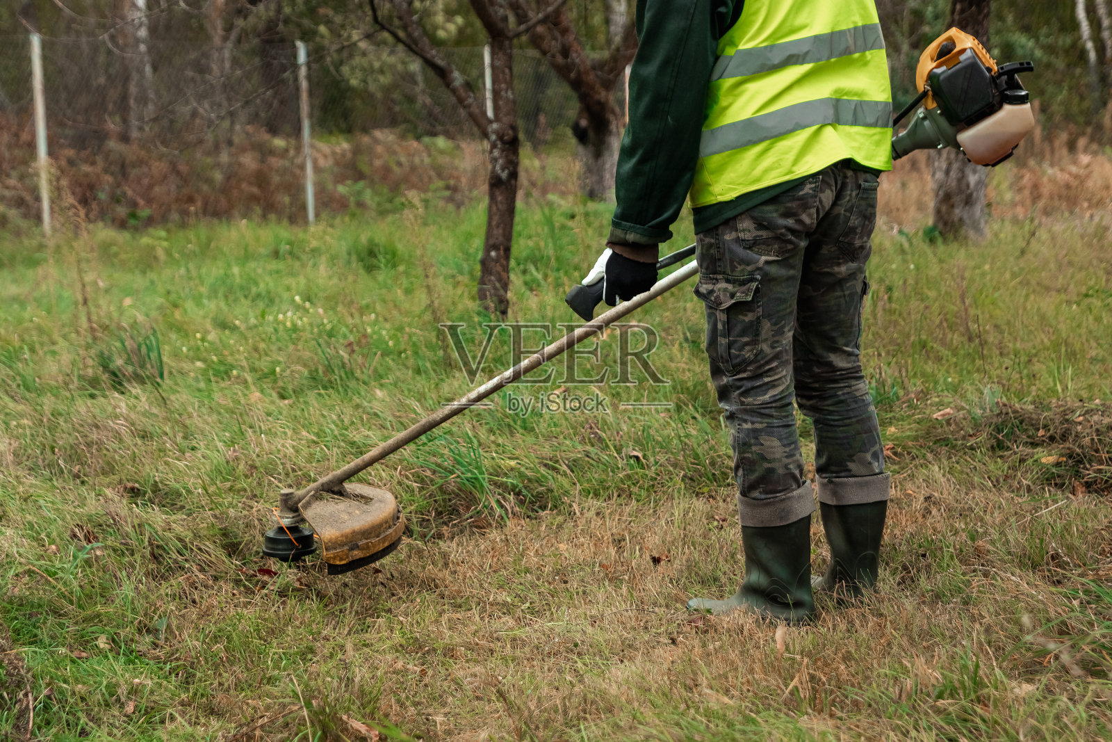 一个穿着专业服装的工人用割草机割草。修剪草坪，路边，边缘照片摄影图片