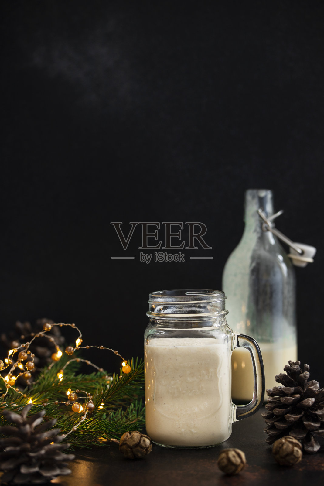 蛋奶酒是传统的圣诞酒精饮料，配肉桂和肉豆蔻。蛋酒在一个罐子和一个瓶子。冬天假日的心情。黑暗的背景。Copyspace。垂直照片摄影图片