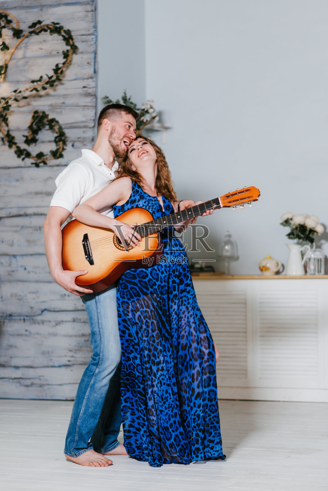 美丽的年轻孕妇和她的丈夫玩吉他。一对夫妇期待着孩子的到来，他们欣喜若狂，大笑不已。照片摄影图片