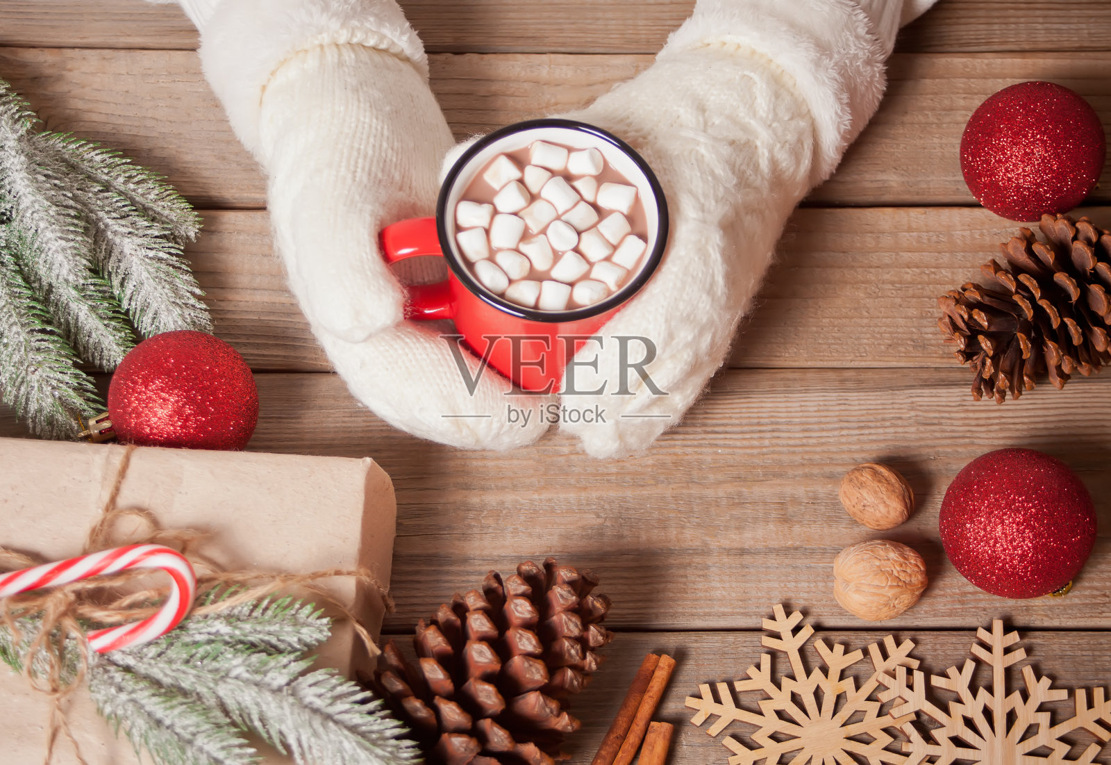 女人戴着白色手套的手拿着红色的带棉花糖的圣诞可可杯。圣诞装饰的背景。照片摄影图片