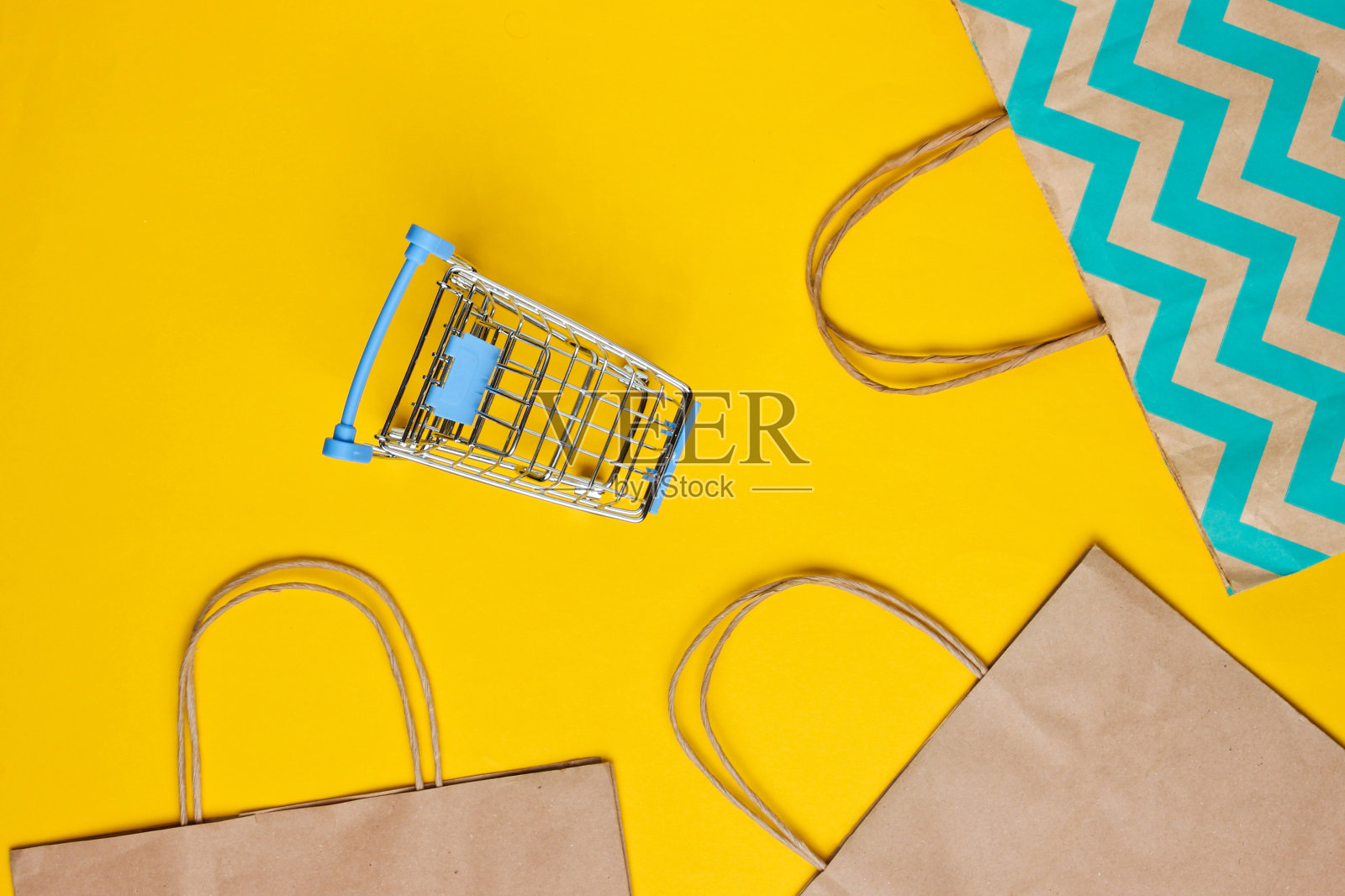 模型与购物车和纸袋在黄色的背景。快乐的客户概念。网上购物。在线商店。消费主义的生活方式照片摄影图片