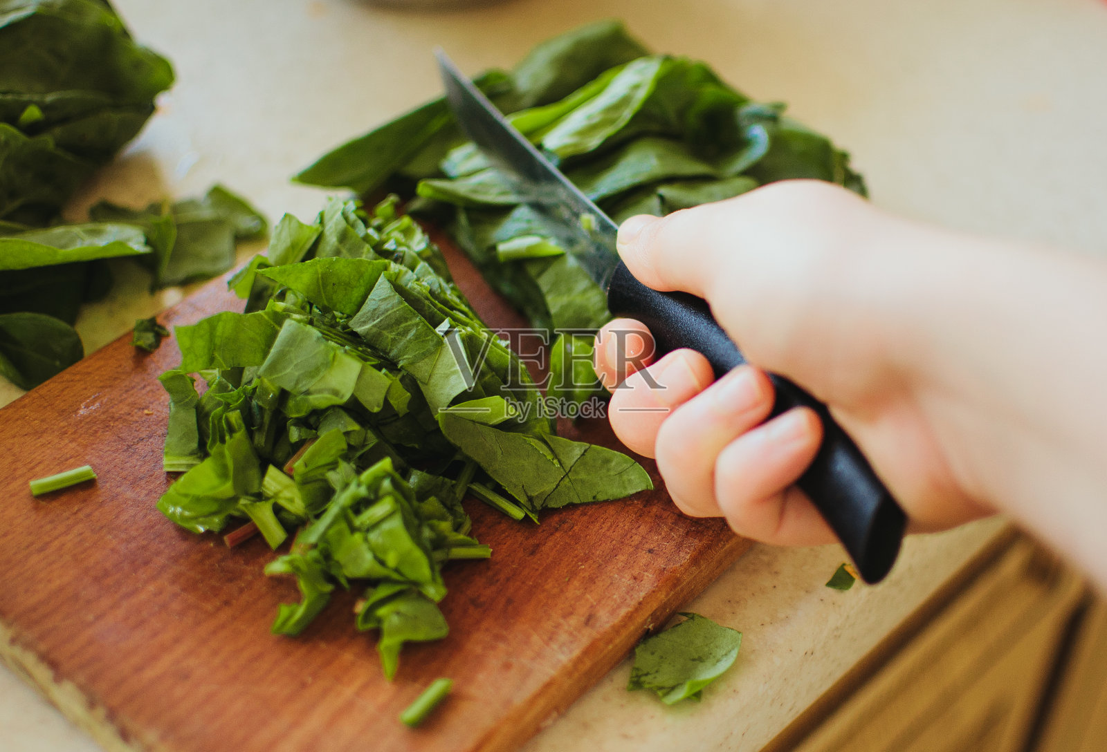 清晨的阳光下，切成片用于罗宋汤和沙拉的年轻绿色酸模放在砧板上，他手里拿着一把乡村风格的刀。副本的空间。照片摄影图片