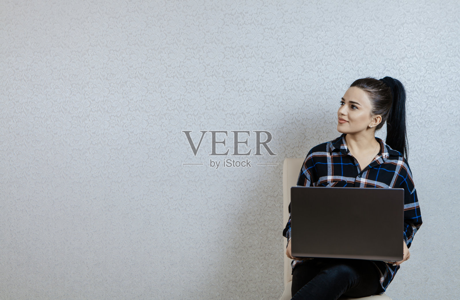 年轻美丽的女孩在灰色的背景和她的手电脑照片摄影图片