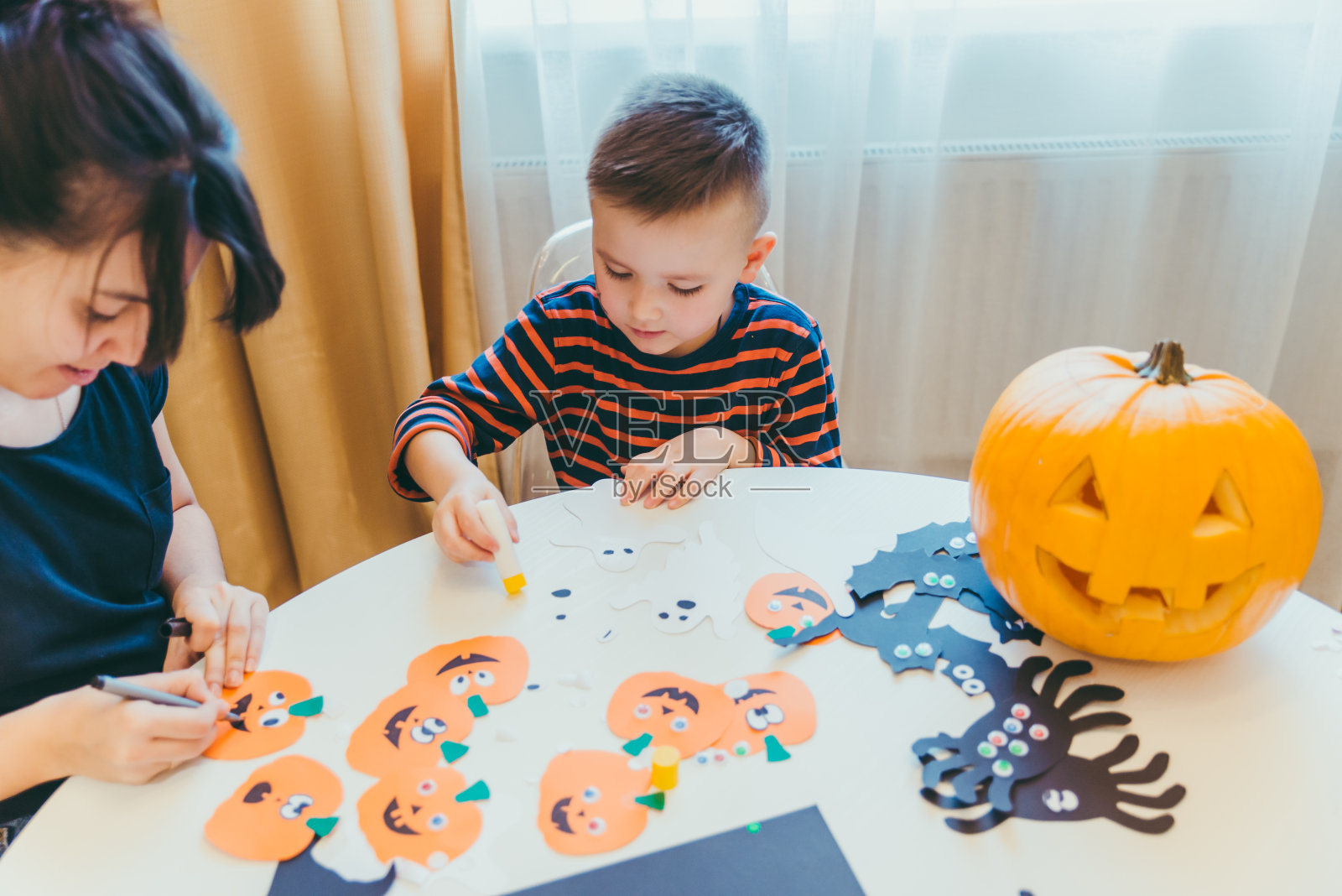 年轻的母亲和蹒跚学步的儿子为万圣节制作工艺南瓜照片摄影图片