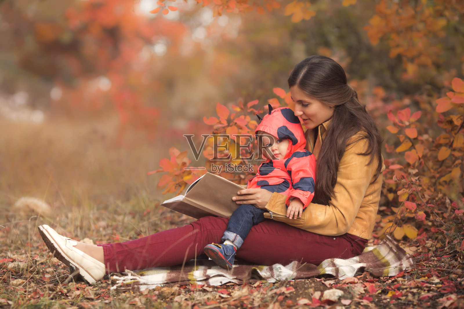快乐的母亲和女儿在秋天公园看书的肖像照片摄影图片