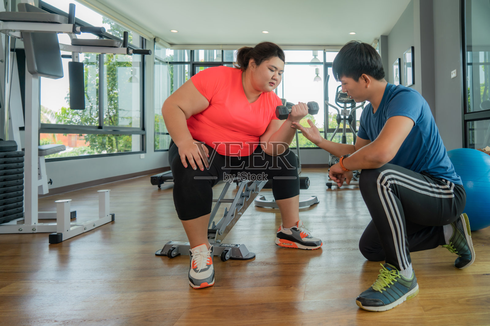 两个亚洲教练男人和超重的女人一起锻炼哑铃在现代健身房，快乐和微笑在锻炼。胖女人注重健康和想减肥的观念。照片摄影图片