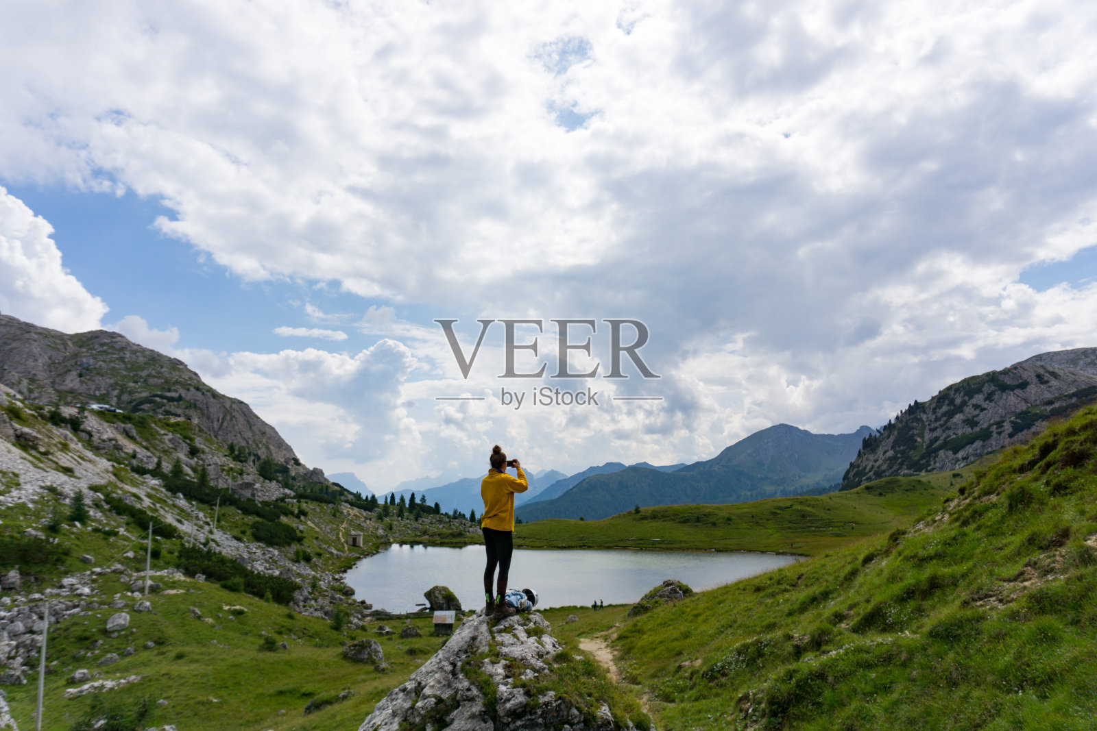 一名女性登山者站在一块大石头上，用手机拍摄风景照片摄影图片