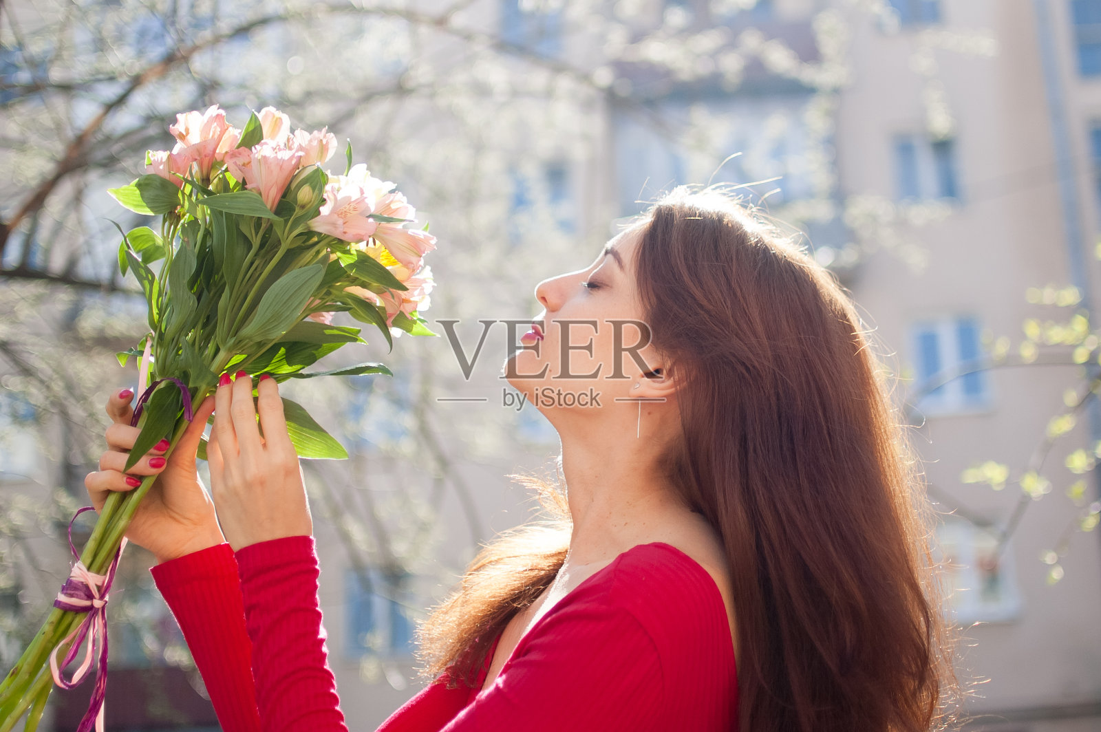 早春时节，可爱的年轻女子收到了一大束五颜六色的花，她正在外面看。照片摄影图片