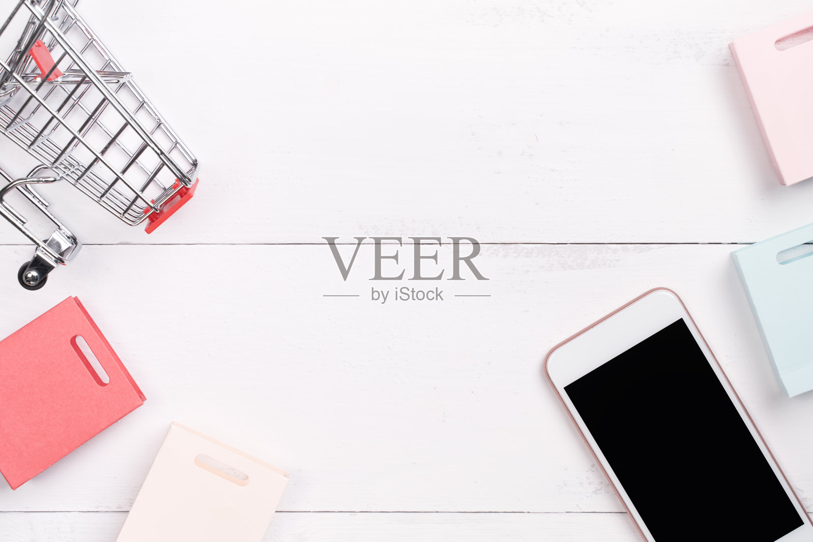 摘要网上购物，移动支付概念设计元素，彩色购物车和纸袋在白色木制桌子的背景。照片摄影图片