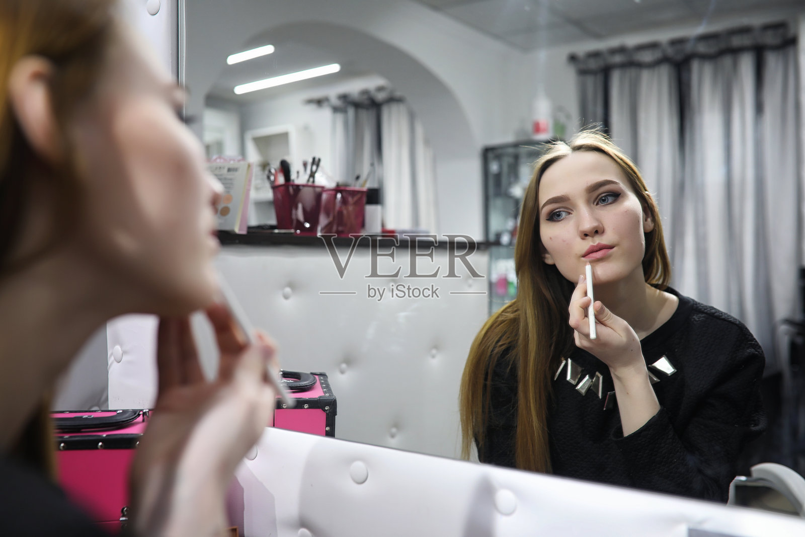 一个年轻的女孩在美容院化妆。镜子前的女孩正在化妆。美容沙龙。照片摄影图片